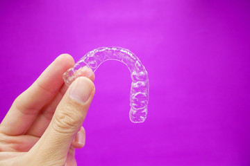 hand holding clear plastic retainer teeth that isolated on purple  background. it's an equipment for orthodontist give the patient to orthodontic surgery in dental clinic or hospital