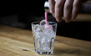 Bartender pouring a strong alcoholic drink into small glasses with ice. Red alcoholic drink. Barman is preparing a cocktail shooter