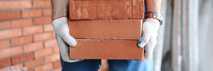 Gloved builder manually carries brick construction