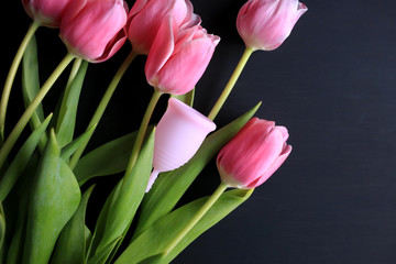 Menstrual cup and pink tulips on a black background. Menstruation, means of protection. Women's health, lifestyle.