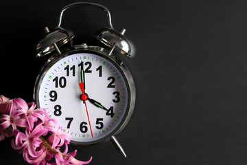 Retro alarm clock with hyacinth flower on a black background. Deadline concept. Spring.