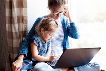 Working mom works from home office with kid. Mother and daughter read news. Woman and cute child...