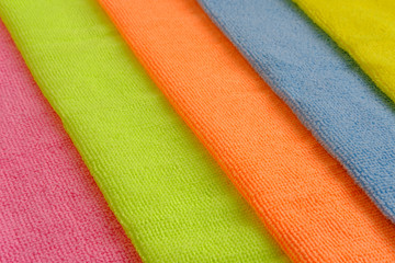 Five rags (towels) of different colors from microfiber to care for glass and glossy surfaces lie diagonally next to each other. Colorful background with side view from above.
