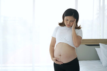 Young asian pregnant woman having headache after getting up from the bed.