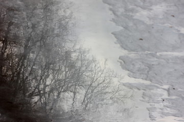 blurred reflection of trees in a spring stream against the background of melting snow