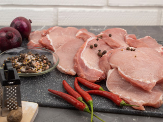 Raw pork steaks on a marble board with spices