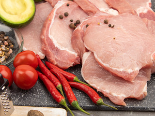 Raw pork steaks on a marble board with spices and vegetables