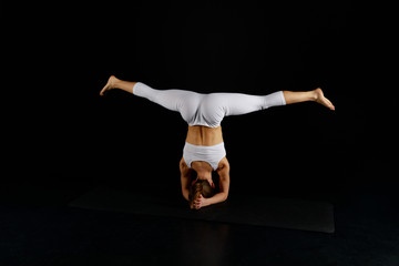 back view of girl in white sportswear doing wide legged headstand isolated on black