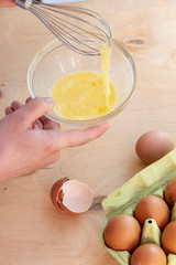 Hands break a raw egg. Stir the protein with the yolk. Glass bowl on a wooden background and a whisk. Cooking.