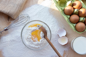 Cooking dough. A raw egg. Stir the protein with the yolk. Sifting flour through a sieve on a wooden background. Glass bowl with mix, towel and wooden spoon.