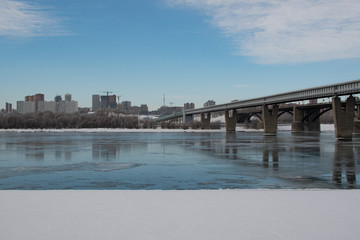 Urban landscape in spring, melting snow on the river, bridge over the river, construction in the...
