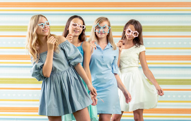 Pretty smiling teenage girls in dresses standing each behind together and holding toy shaped...