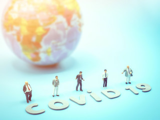 A group of miniature businessmen stand in front of the earth globe negotiating international trade cooperation, during crisis covid-19. Business, economy, healthcare concept