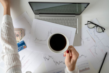 Woman freelancer with banknotes fifty U.S. dollars and credit card. counting profit, income. laptop, graphics and charts printed on the paper on office table. Forex exchange. Flat lay