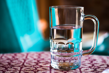  Fresh drinking water without alcohol in transparent glass on a table against blur coral green background. Concept of natural healthy drinks to maintain health and fitness.