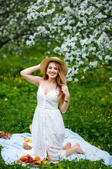 Obraz premium A positive lady in a hat and sundress laughs against the background of a blooming Apple tree. An optimistic woman in a wide smile in the garden. Spring time