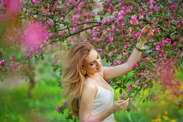 Naklejka premium Beautiful teen redhead girl enjoying life in spring blossoming garden against blooming trees. Young dreamy thoughtful lady in nature at sunset. Springtime at countryside concept