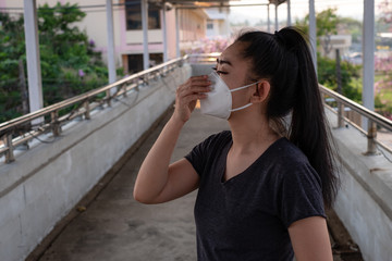 Close up of a woman standing putting on a respirator N95 mask to protect from airborne respiratory diseases as the flu covid-19 coronavirus ebola PM2.5 dust and smog on the road burred background