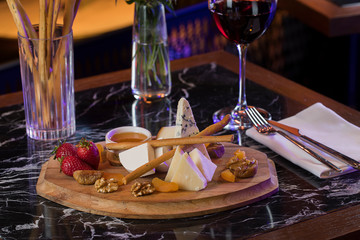 cheese plate with cheese with mold crackers, strawberry and nuts with red wine