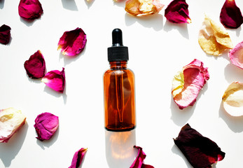 Bottles of aromatic oil with rose petals on a white background. Basics of aromatherapy. Top view. Botanical skin care home Spa treatment.