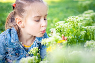 Little pretty girl blowing dandelion flowers in green park