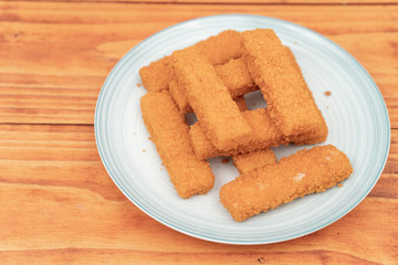 Fried fish sticks on the plate above wooden background
