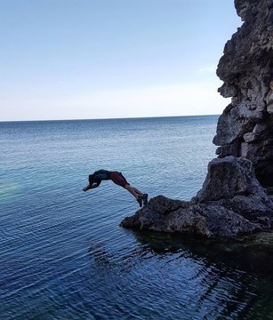 Woman Diving From Cliff In Sea