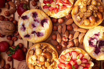 Mini tarts cupcakes with strawberries, walnuts, almond, nuts and blueberries on wooden background. Top view. Close up