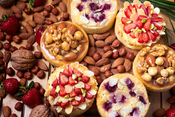Mini tarts cupcakes with strawberries, walnuts, almond, nuts and blueberries on wooden background. Top view. Close up
