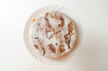 Homemade tender charlotte (apple pie) sprinkled with powdered sugar on a wooden stand.
