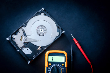 Repair of open computer hard disk drive and usage of digital multimeter, closeup with text space