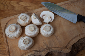 Common white mushrooms on a chopping board with a knife