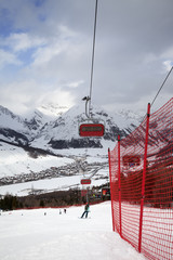 Chair-lift, snowy ski slope with snowboarders and skiers in high mountains