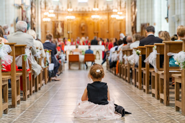 Little girl sitting in the central aisle of a church during the wedding ceremony
