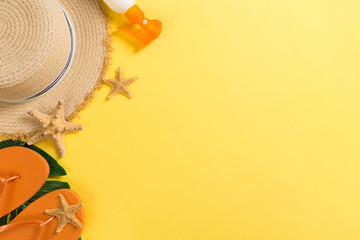 Beach accessories with straw hat, sunscreen bottle and seastar on yellow background top view with...