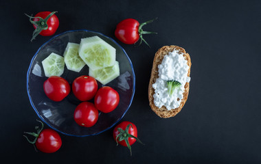 Cherry tomatoes, cucumbers, sandwiches with cottage cheese on  black table
