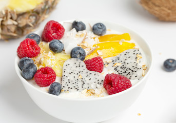 Healthy breakfast Smoothie bowl with mango, pineapple, dragon fruit, blueberries, raspberries and coconut. Tasty summer breakfast.