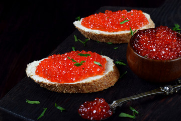 Naklejka na ściany i meble Sandwiches with red caviar, bran bread and butter on the black wooden board