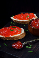 Sandwiches with red caviar, bran bread and butter on the black wooden board
