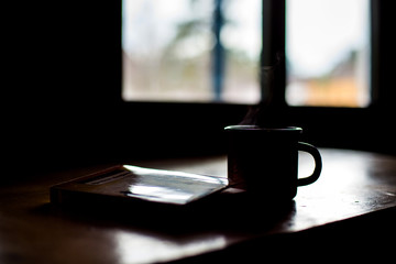 early morning, a Cup of coffee is on a wooden table, and a book is lying next to it