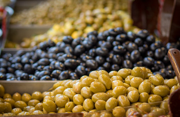 Pile of pickled green olives, in a metal bowl, shallow depth of field, in the background of black olives, Mahane Yehuda Market, Jerusalem.