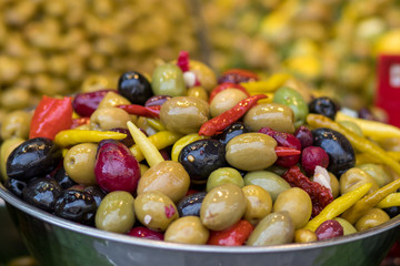 A pile of pickled olives from different varieties. Mix with hot peppers, in a metal bowl. Blurred background. Arabic style. The Old Market, Jerusalem.
