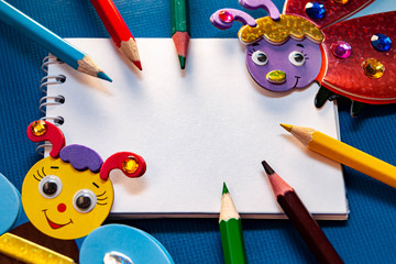 детский рисунок, творчество, разноцветные карандаши и букашки и белый блокнот на синем фоне