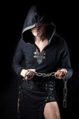 Young man posing in hooded gothic clothes with chain in hands