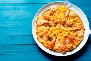 Seafood pizza with shrimp, Mussels, Crab Sticks and Hokkaido Cheese, Isolated on white plate, Top view on the blue wood texture with natural patterns background with naturday light  in summer.