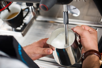 Coffee shop worker preparing coffee on steam espresso coffee machine. Cropped shot of man working in coffee shop wearing an apron.