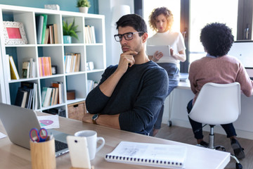 Handsome young entrepreneur using the laptop while his colleagues working together in the office.
