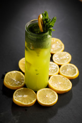 Bright green lemonade cocktail garnished with lemon and mint on black background
