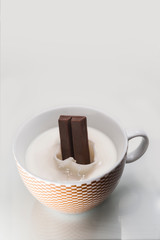 Chocolate bar falling and splashing into a cup of milk.