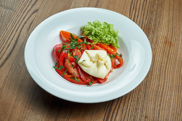 Vegetarian salad with tomatoes, parsley, green onions, khinkali and bell pepper in a white bowl on a wooden background. Georgian style salad. Close up